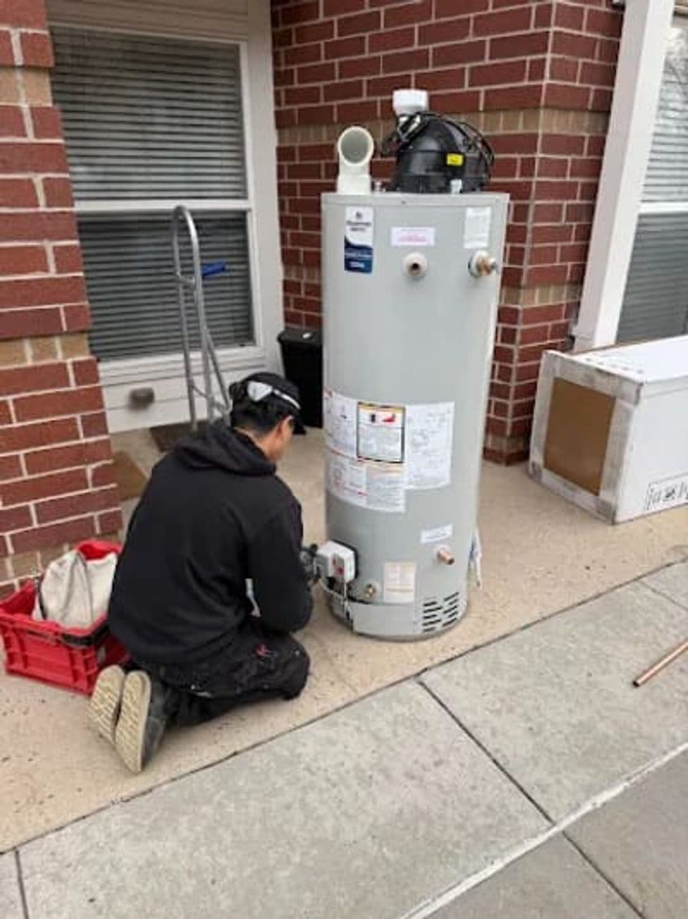 Technician installing a water heater outside a home on a concrete surface.