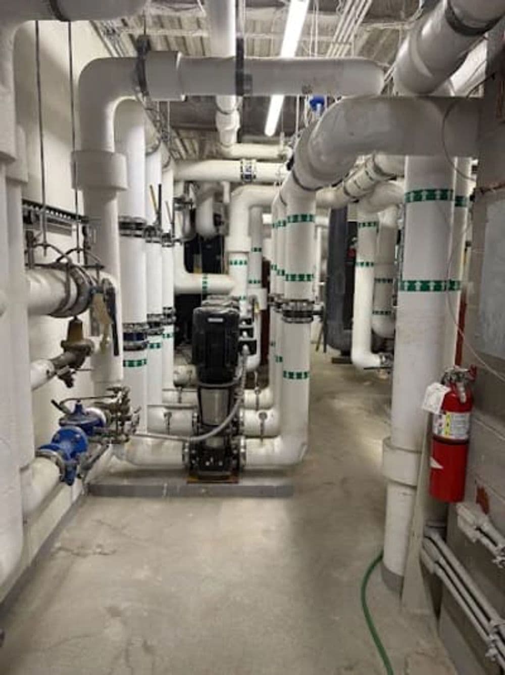 Industrial utility room featuring extensive pipe systems and a pump, well-lit and organized.