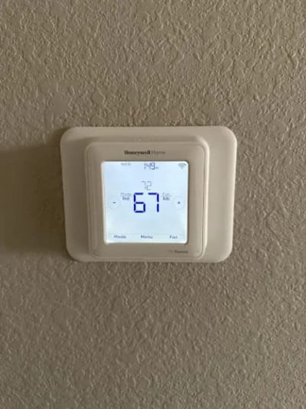 Smart thermostat displaying a temperature setting of 67 degrees Fahrenheit on a wall.