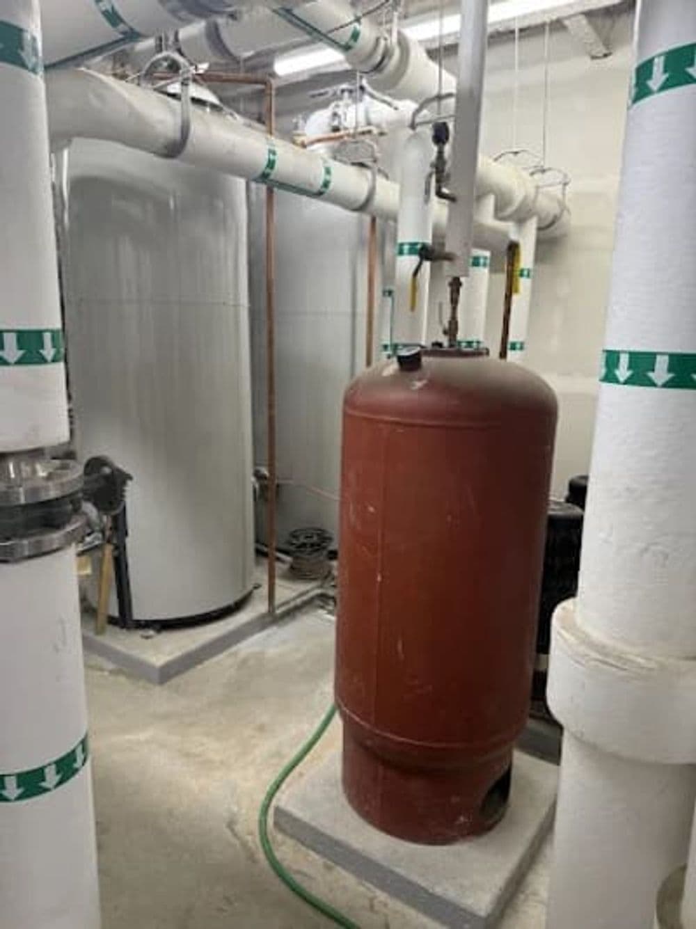 Industrial basement with red pressure tank and pipes for plumbing and heating systems.