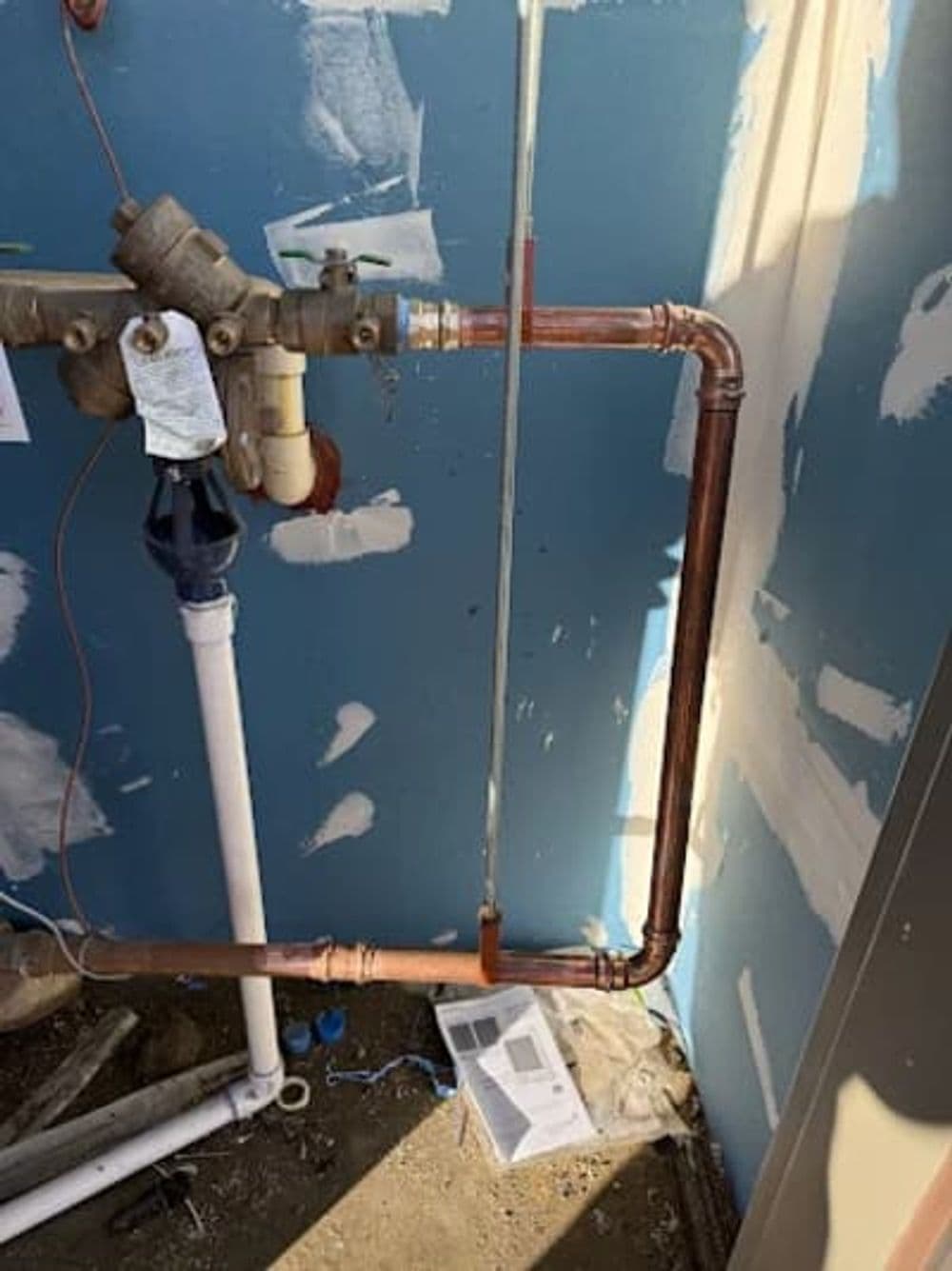 Copper plumbing pipes installed against a blue wall in a construction setting.