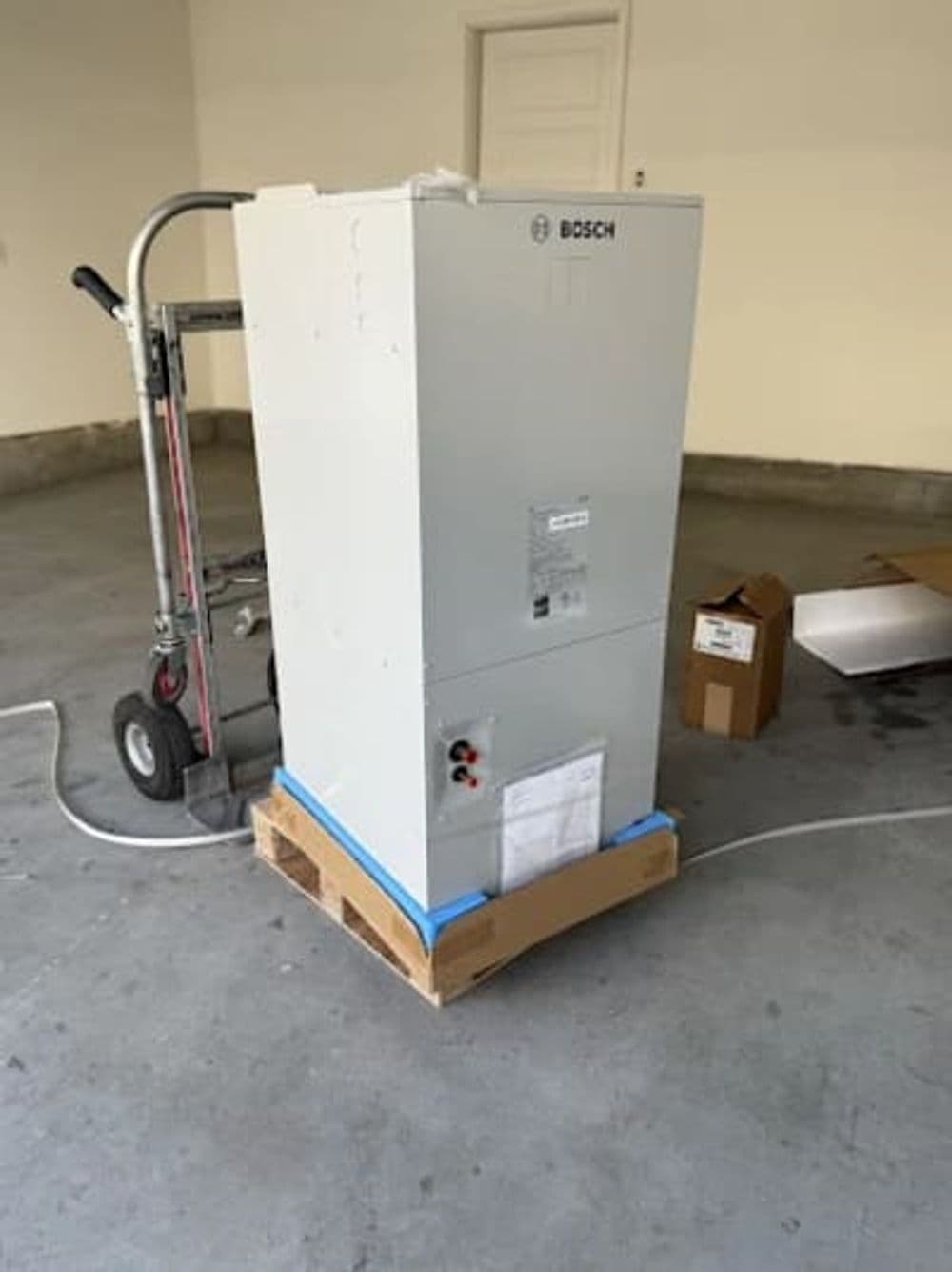 Bosch heating unit on a pallet in a garage, with a hand truck and cardboard boxes nearby.